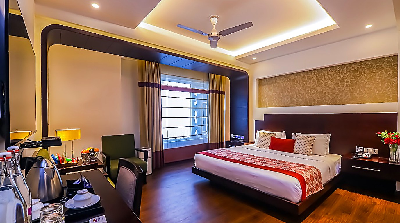 Godwin Hotels luxury boutique designer room suite featuring king plush bed, red geometric runner, ambient recessed cove lighting, and executive tea workstation in New Delhi